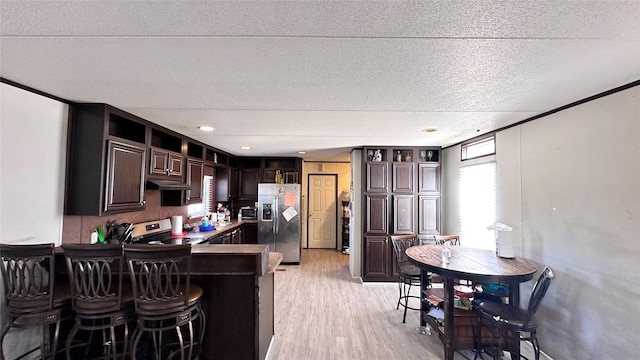 kitchen featuring dark brown cabinetry, appliances with stainless steel finishes, a breakfast bar, a textured ceiling, and light wood-style flooring