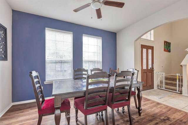 dining room featuring ceiling fan, arched walkways, light wood-style flooring, baseboards, and stairway