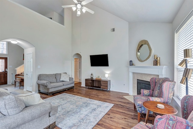living area featuring a ceiling fan, wood finished floors, a fireplace, high vaulted ceiling, and arched walkways