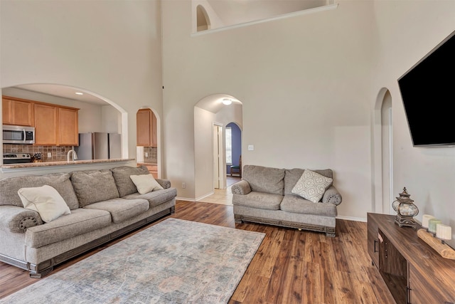 living room featuring arched walkways, a high ceiling, baseboards, and dark wood-type flooring