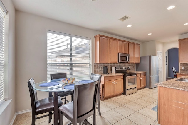 kitchen with visible vents, appliances with stainless steel finishes, tasteful backsplash, light stone countertops, and arched walkways