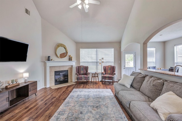 living room with ceiling fan, arched walkways, wood finished floors, a tile fireplace, and visible vents