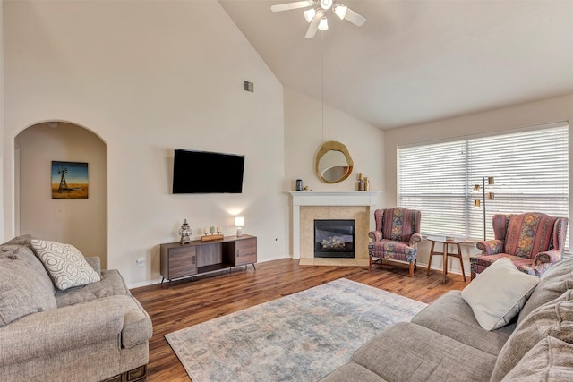 living area with ceiling fan, visible vents, a tiled fireplace, wood finished floors, and high vaulted ceiling
