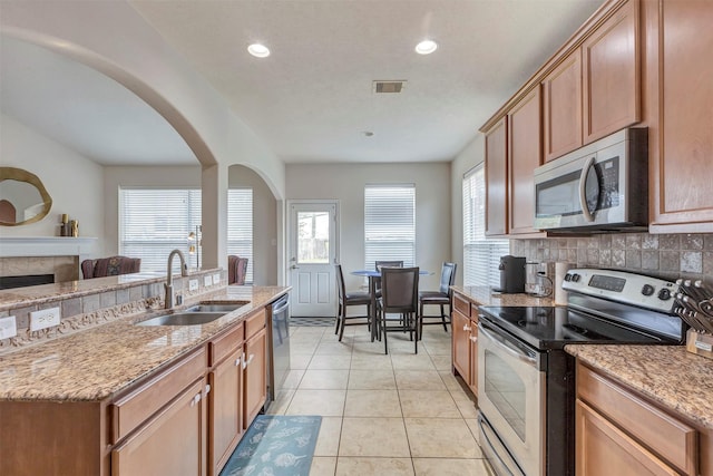 kitchen with light stone counters, a sink, arched walkways, stainless steel appliances, and visible vents