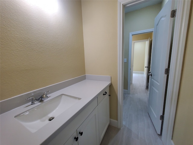 bathroom featuring baseboards, a textured wall, wood finished floors, and vanity