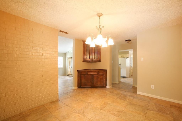 empty room with a textured ceiling, an inviting chandelier, visible vents, and brick wall