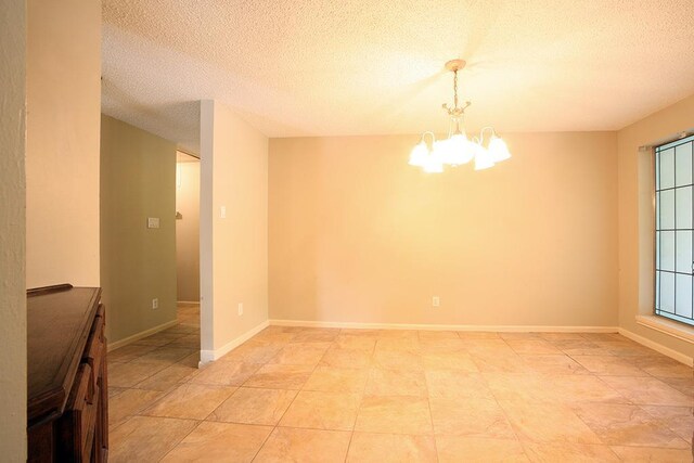 empty room with a textured ceiling, a chandelier, and baseboards
