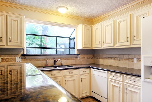 kitchen featuring a textured ceiling, dark countertops, a sink, white appliances, and cream cabinetry