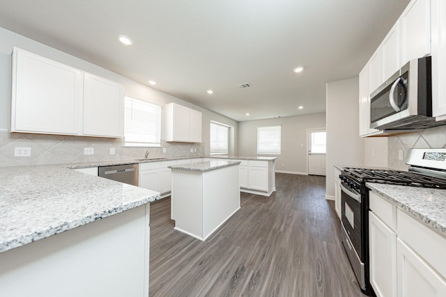 kitchen with appliances with stainless steel finishes, backsplash, wood finished floors, and white cabinetry