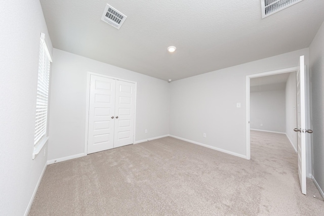 unfurnished bedroom featuring visible vents, baseboards, a closet, and light colored carpet