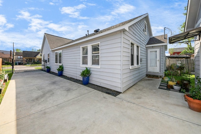 view of side of home with fence, a patio, a shingled roof, a gate, and driveway