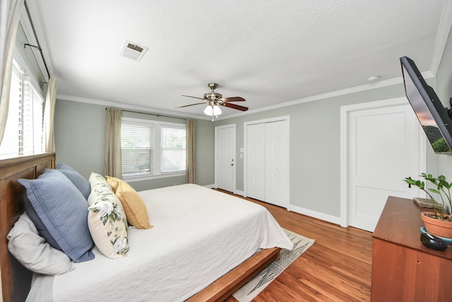 bedroom featuring visible vents, crown molding, wood finished floors, two closets, and baseboards