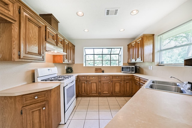 kitchen featuring white gas range oven, a sink, stainless steel microwave, under cabinet range hood, and visible vents