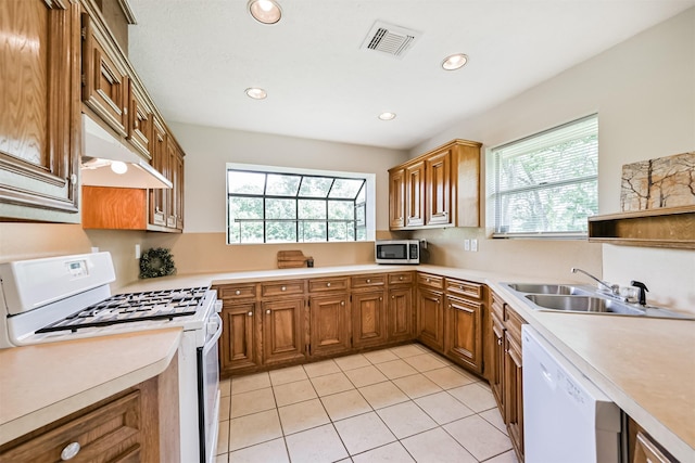 kitchen with white appliances, under cabinet range hood, brown cabinets, and visible vents
