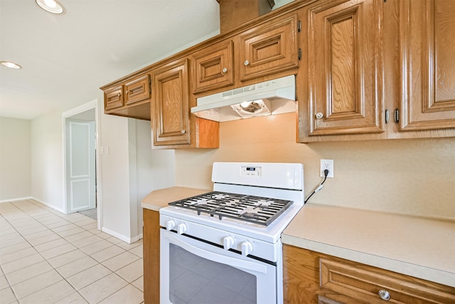 kitchen with brown cabinetry, light countertops, baseboards, under cabinet range hood, and white range with gas stovetop