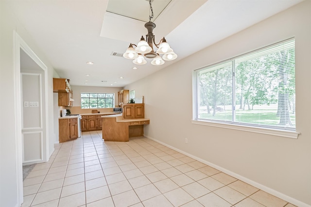 kitchen featuring brown cabinetry, a peninsula, baseboards, light countertops, and a notable chandelier