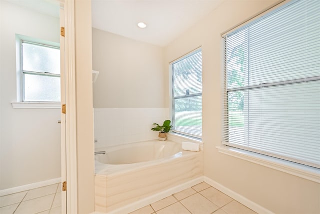 bathroom featuring tile patterned flooring, baseboards, a bath, and a healthy amount of sunlight