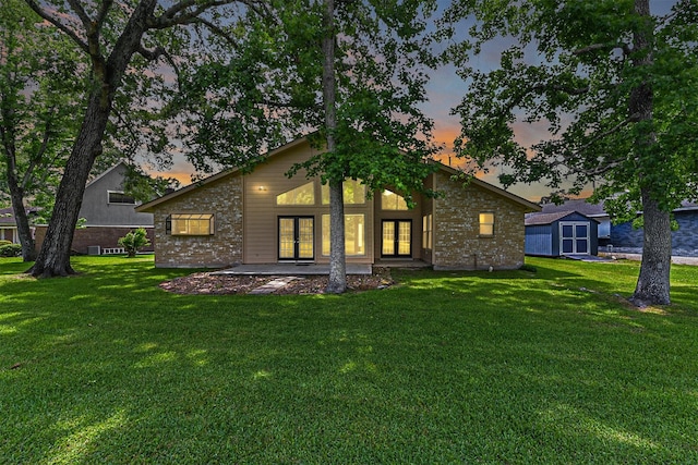 back of property at dusk featuring an outdoor structure, a shed, french doors, brick siding, and a yard