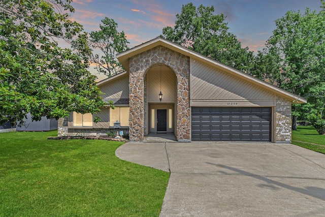 view of front facade featuring an attached garage, stone siding, driveway, and a front yard