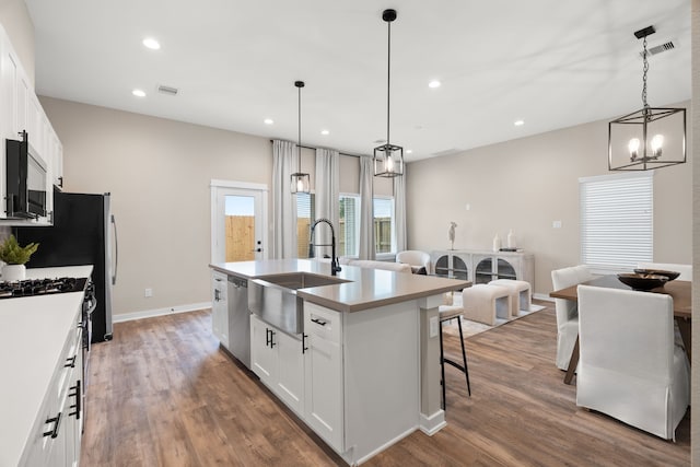 kitchen featuring appliances with stainless steel finishes, a sink, an island with sink, white cabinetry, and wood finished floors