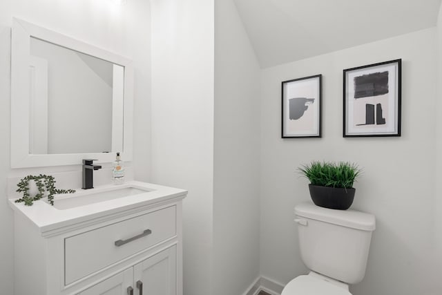half bath featuring toilet, baseboards, vaulted ceiling, and vanity
