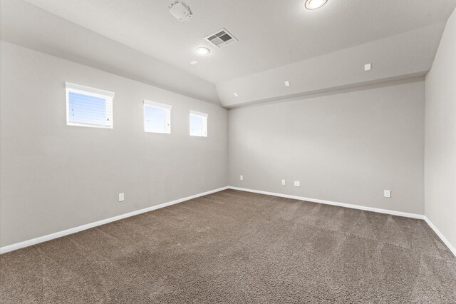 empty room featuring visible vents, baseboards, vaulted ceiling, and dark colored carpet