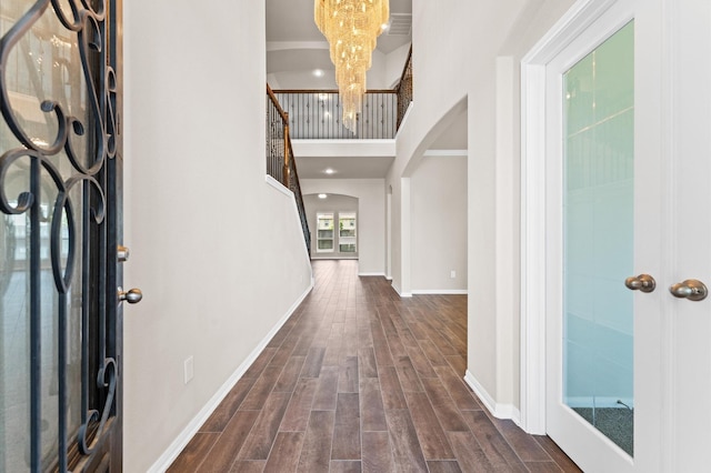 foyer featuring arched walkways, dark wood finished floors, baseboards, a notable chandelier, and a high ceiling