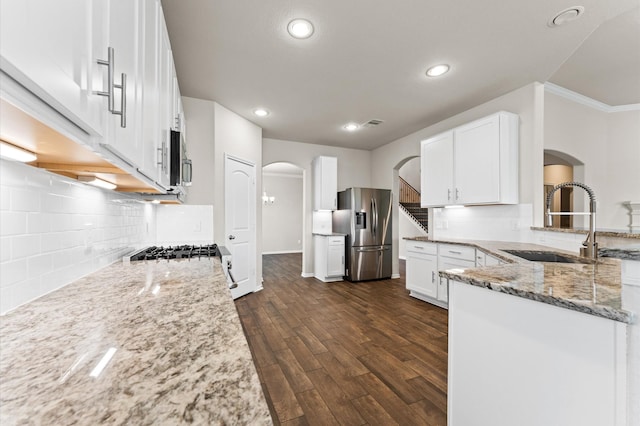 kitchen with appliances with stainless steel finishes, light stone counters, a sink, arched walkways, and recessed lighting