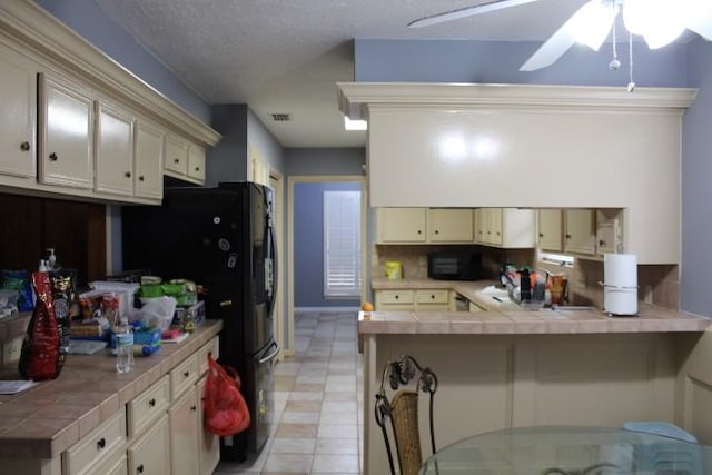 9222 Chesney Downs Dr, Houston, TX 77083 - kitchen with tile countertops, a peninsula, cream cabinets, freestanding refrigerator, and ceiling fan