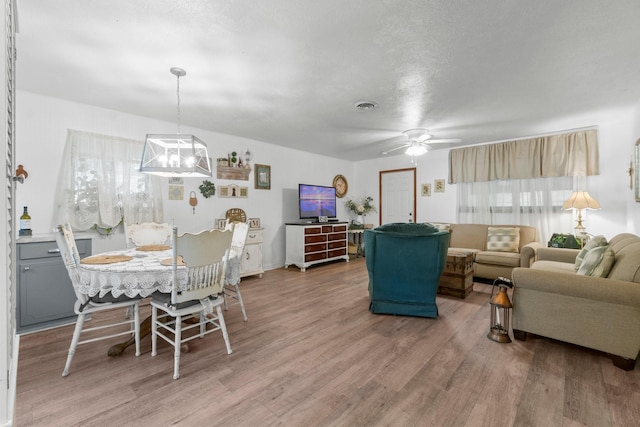 living area featuring light wood-style floors, ceiling fan with notable chandelier, and visible vents