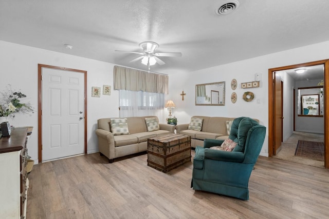 living room featuring a ceiling fan, visible vents, and light wood finished floors