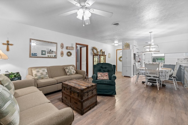 living area with a ceiling fan, visible vents, and wood finished floors