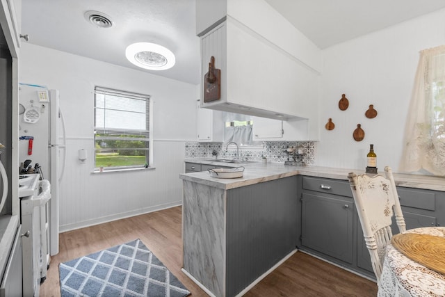 kitchen with gray cabinets, visible vents, a sink, a peninsula, and dark wood-style floors