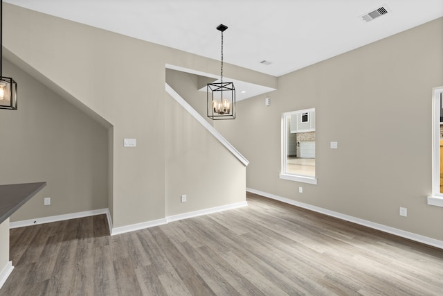 unfurnished living room featuring a notable chandelier, baseboards, visible vents, and wood finished floors