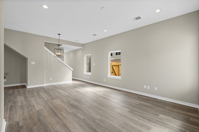 unfurnished living room featuring visible vents, baseboards, wood finished floors, and a notable chandelier