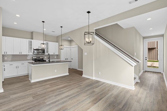kitchen with white cabinets, light wood finished floors, stainless steel appliances, backsplash, and glass insert cabinets