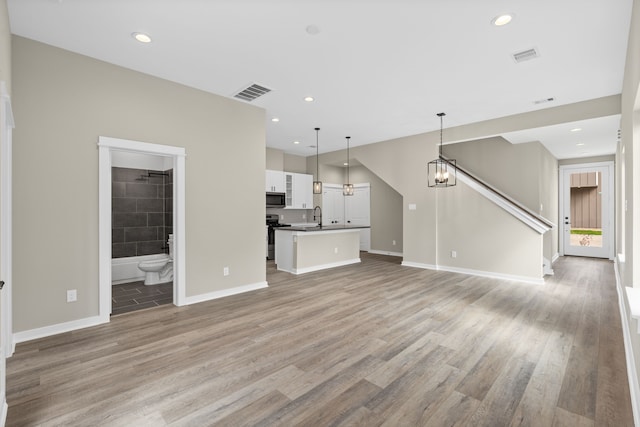 unfurnished living room with visible vents, a sink, and light wood finished floors