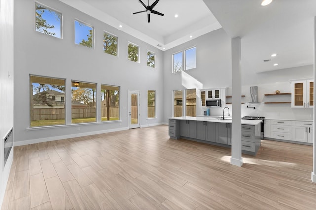 unfurnished living room with a sink, a high ceiling, recessed lighting, a ceiling fan, and light wood finished floors