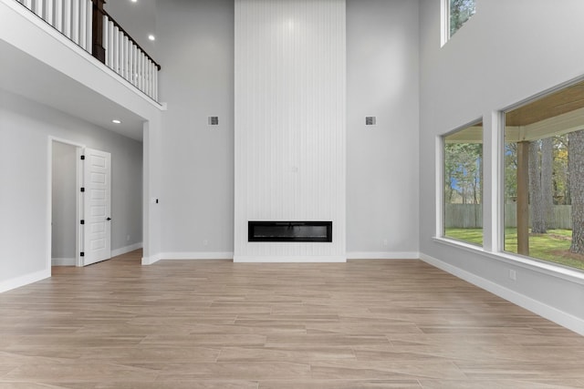 unfurnished living room featuring a large fireplace, baseboards, and a towering ceiling