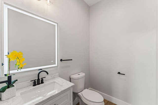 half bathroom with vanity, baseboards, and toilet