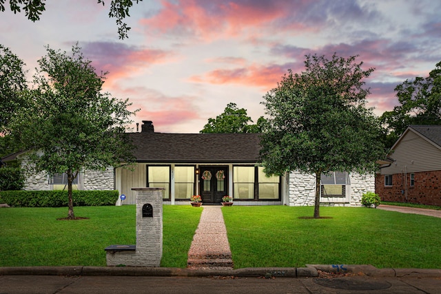ranch-style home featuring a chimney, a front lawn, french doors, and stone siding
