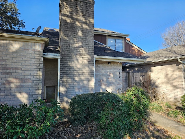 view of home's exterior featuring brick siding, a shingled roof, and a chimney