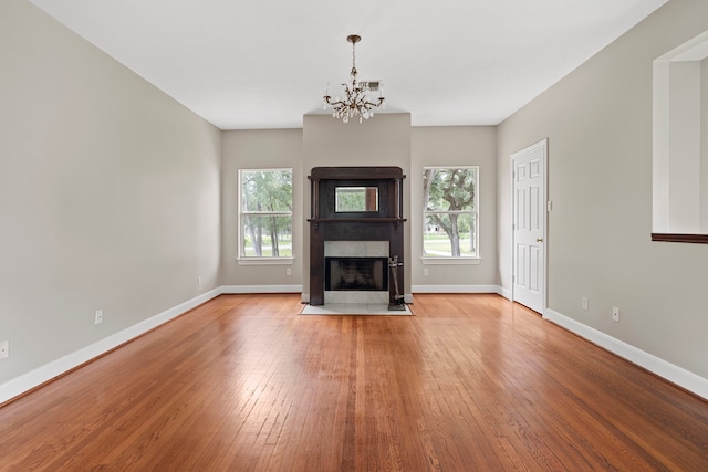 unfurnished living room with an inviting chandelier, a fireplace with flush hearth, a healthy amount of sunlight, and hardwood / wood-style flooring