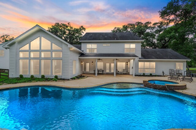 back of property at dusk featuring a patio, ceiling fan, and a pool with connected hot tub