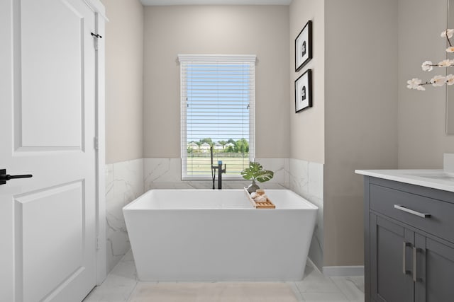 bathroom with vanity, marble finish floor, a freestanding tub, tile walls, and a wainscoted wall