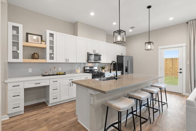kitchen with a sink, light wood-style floors, an island with sink, stainless steel appliances, and backsplash