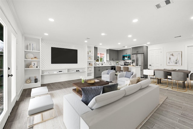 living area with wood finish floors, built in features, recessed lighting, visible vents, and ornamental molding