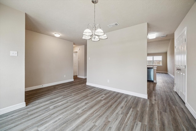 unfurnished room with baseboards, visible vents, wood finished floors, and a chandelier