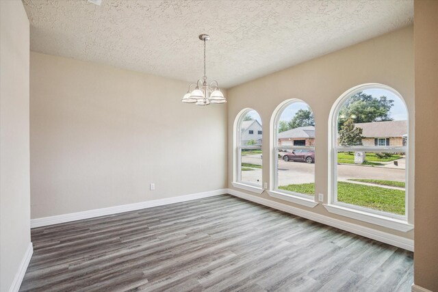unfurnished room featuring plenty of natural light, a textured ceiling, a chandelier, and dark wood finished floors