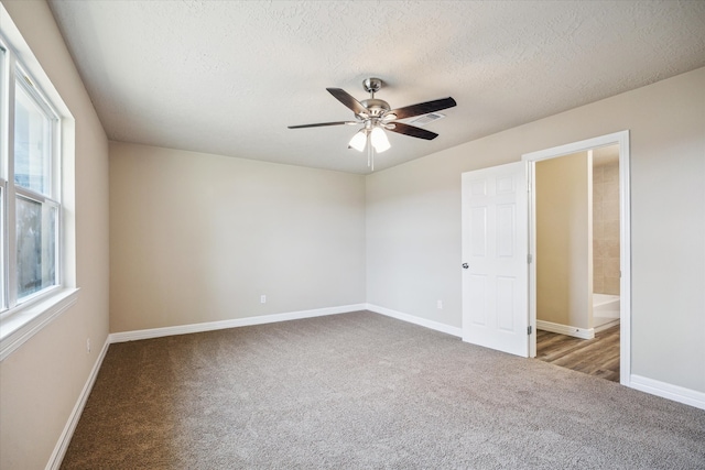 carpeted empty room with baseboards, a textured ceiling, ceiling fan, and visible vents